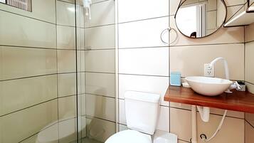 A bathroom with a glass shower enclosure, a white toilet, a sink with a mirror above it, and a blue soap dish.