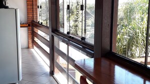 A kitchen with a refrigerator, a dining area with a table and chairs, and large windows with a view of greenery outside.