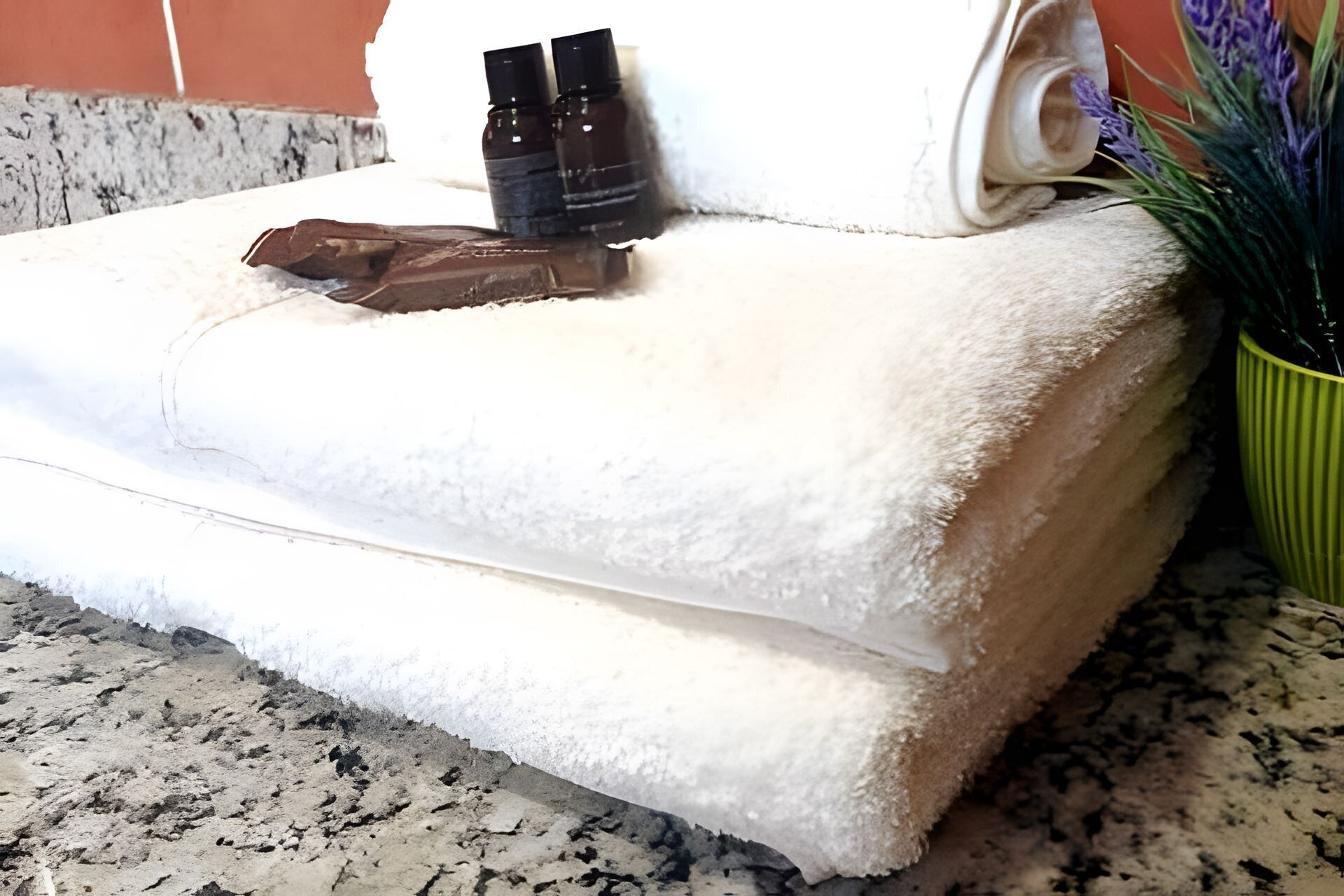 A stack of white towels on a granite countertop with a green plant and two small bottles on top.