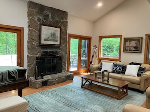 A living room with a stone fireplace, a sofa, a coffee table, and large windows.
