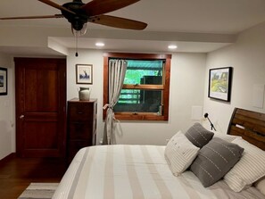 A bedroom with a bed, a ceiling fan, a window with curtains, a wooden door, and a dresser.