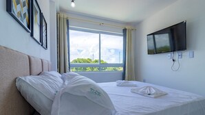 Habitación de hotel con cama, televisor montado en la pared y ventana con cortinas.