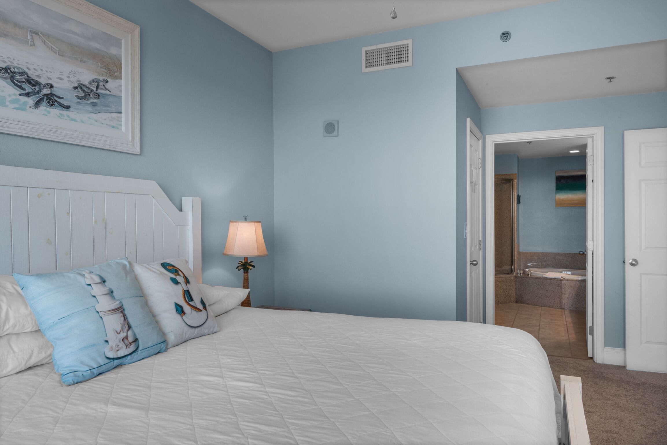 A bedroom with a bed, pillows, a nightstand, a lamp, and a painting on the wall.