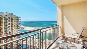 A balcony with a view of the ocean, a pool, and a building with multiple balconies.