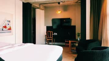 Habitación de hotel con cama, escritorio, silla, televisor y planta.