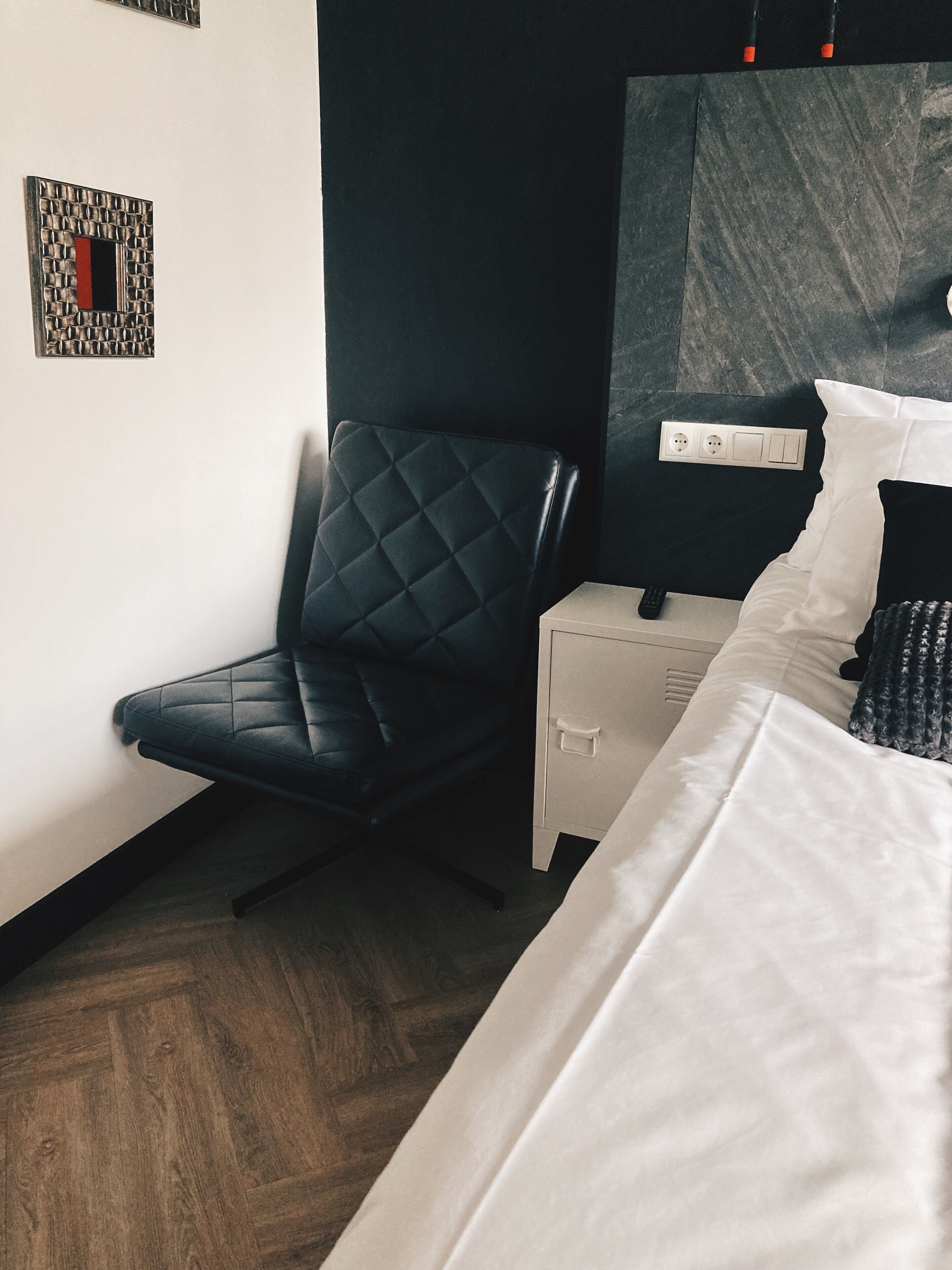 Habitación de hotel moderna con una silla de cuero negro, una mesita de noche blanca, una cama con ropa de cama blanca y un cabecero de mármol.