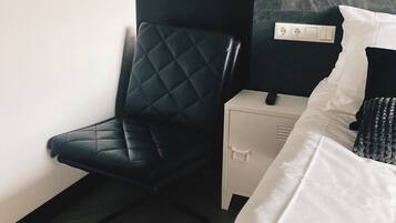 Habitación de hotel moderna con una silla de cuero negro, una mesita de noche blanca, una cama con ropa de cama blanca y un cabecero de mármol.
