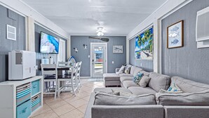Ein Wohnzimmer mit grauem Sofa, einem Fernseher, einem Deckenventilator und Kunstwerken an den Wänden.