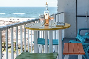 Un balcon avec une table dressée pour deux personnes, une bouteille de vin et des verres. La vue comprend l’océan et une plage.
