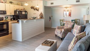 Eine moderne Küche mit weißen Schränken, einem schwarzen Kühlschrank und einer Holztischinsel. Es gibt einen Essbereich mit gestreiften Stühlen und einem grauen Sofa.
