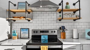 A kitchen with a stainless steel stove, white cabinets, and a tiled backsplash. There are wooden shelves above the stove and a framed picture on the wall. - 5 bed 4 bath pool table, fire pit, walk to beach (Daytona Beach)