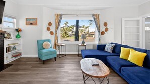 A living room with a blue sofa, a teal armchair, a coffee table, and a window with curtains. - 5 bed 4 bath pool table, fire pit, walk to beach (Daytona Beach)