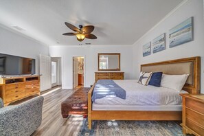 A bedroom with a large bed, wooden headboard, a ceiling fan, a TV, and a bench. - Excellent Management Steps From Beach Pool (Destin)