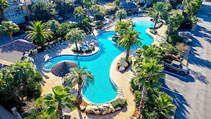 An aerial view of a resort with a large, winding pool surrounded by palm trees and lounge chairs. - Excellent Management Steps From Beach Pool (Destin)