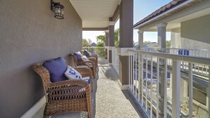 A covered balcony with wicker chairs and cushions, a white railing, and a clear view of the surroundings. - Excellent Management Steps From Beach Pool (Destin)