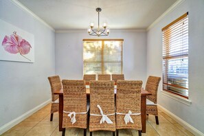 A dining area with wicker chairs, a chandelier, and a window with blinds. - Excellent Management Steps From Beach Pool (Destin)
