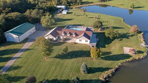 An aerial view of a house with a large lawn, a swimming pool, and a pond.