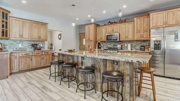 A modern kitchen with wooden cabinets, a large island with stools, stainless steel appliances, and pendant lighting.