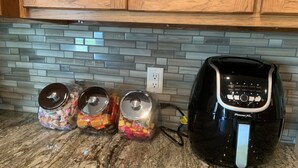A kitchen with a granite countertop, three glass jars with metal lids, and a black coffee maker labeled "PowerXL" plugged in.