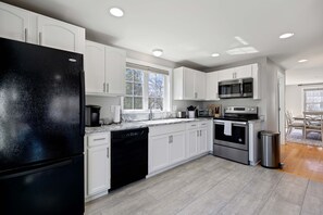 Una cocina moderna con armarios blancos, un refrigerador negro, electrodomésticos de acero inoxidable y un ventanal que proporciona luz natural.