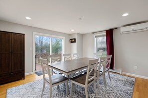 Un comedor con una mesa de madera y sillas blancas, un aparador de madera oscura y una alfombra estampada.
