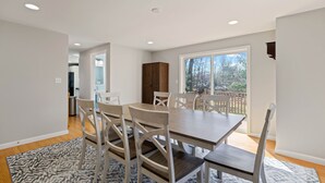 Comedor con una mesa grande y sillas, cocina al fondo y vistas al exterior.