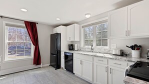 Una cocina moderna con armarios blancos, un refrigerador negro, un lavavajillas y un ventanal con cortina roja.