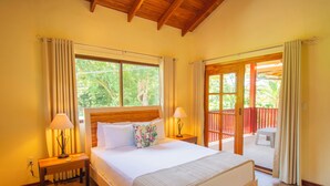 A bedroom with a wooden headboard, a bed with white bedding, two bedside lamps, and a view of a balcony with a wooden railing.