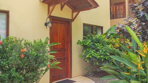 A wooden door with a porch, surrounded by lush greenery and a tiled entrance area.