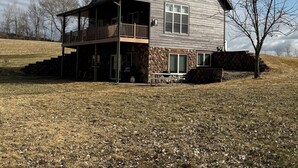 A two-story house with a balcony, stone foundation, and a grassy yard. - Quiet, secluded bluff top cabin with beautiful sunsets (Alma)