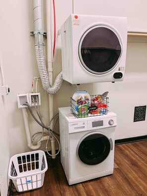 Een wasruimte met een wasmachine, een droger en een technische ruimte met een stopknop.