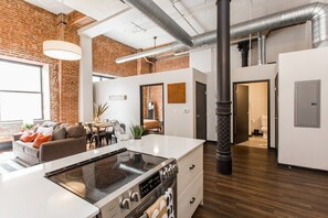 Une cuisine moderne dotée d’un grand îlot central, d’appareils électroménagers en acier inoxydable et d’un mur en briques.