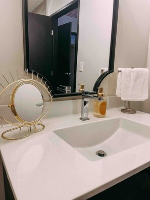 Een badkamer met een witte wastafel, een spiegel met gouden lijst, een zwarte kraan en een witte handdoek aan de muur.