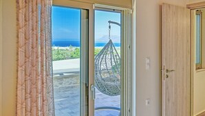 Een glazen schuifdeur die leidt naar een balkon met een hangstoel en uitzicht op de oceaan.