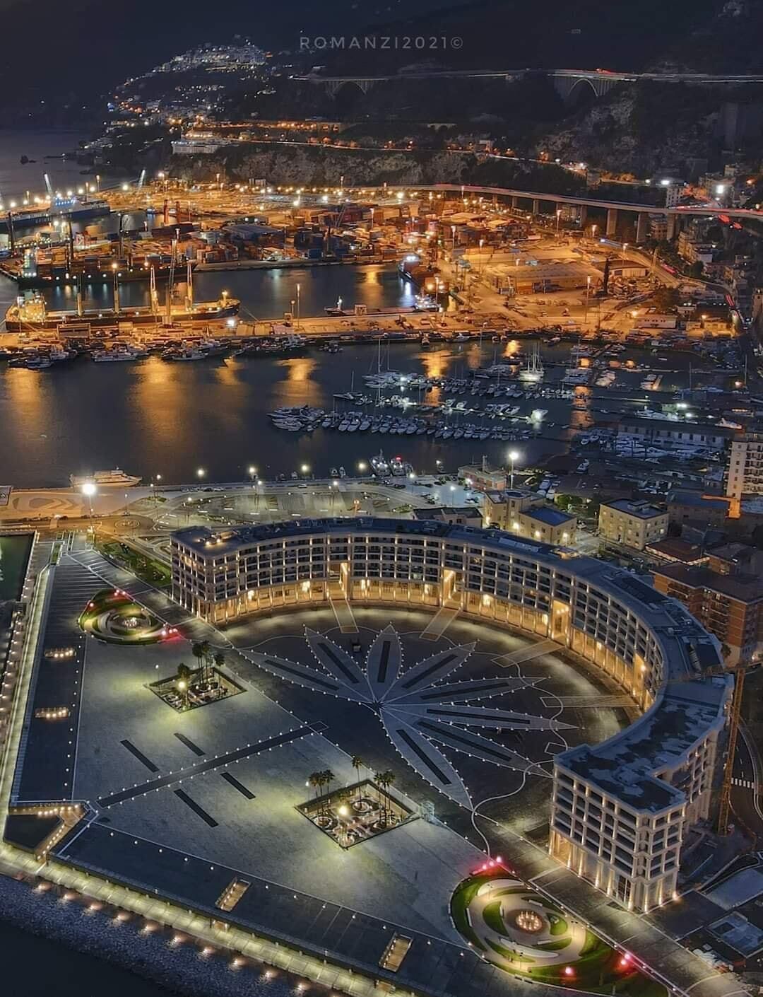 An aerial view of a marina with boats docked, a roundabout, and surrounding buildings.