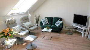 Una sala de estar moderna con tragaluz, un sofá gris, un sofá verde, una mesita blanca y un televisor sobre un mueble blanco.