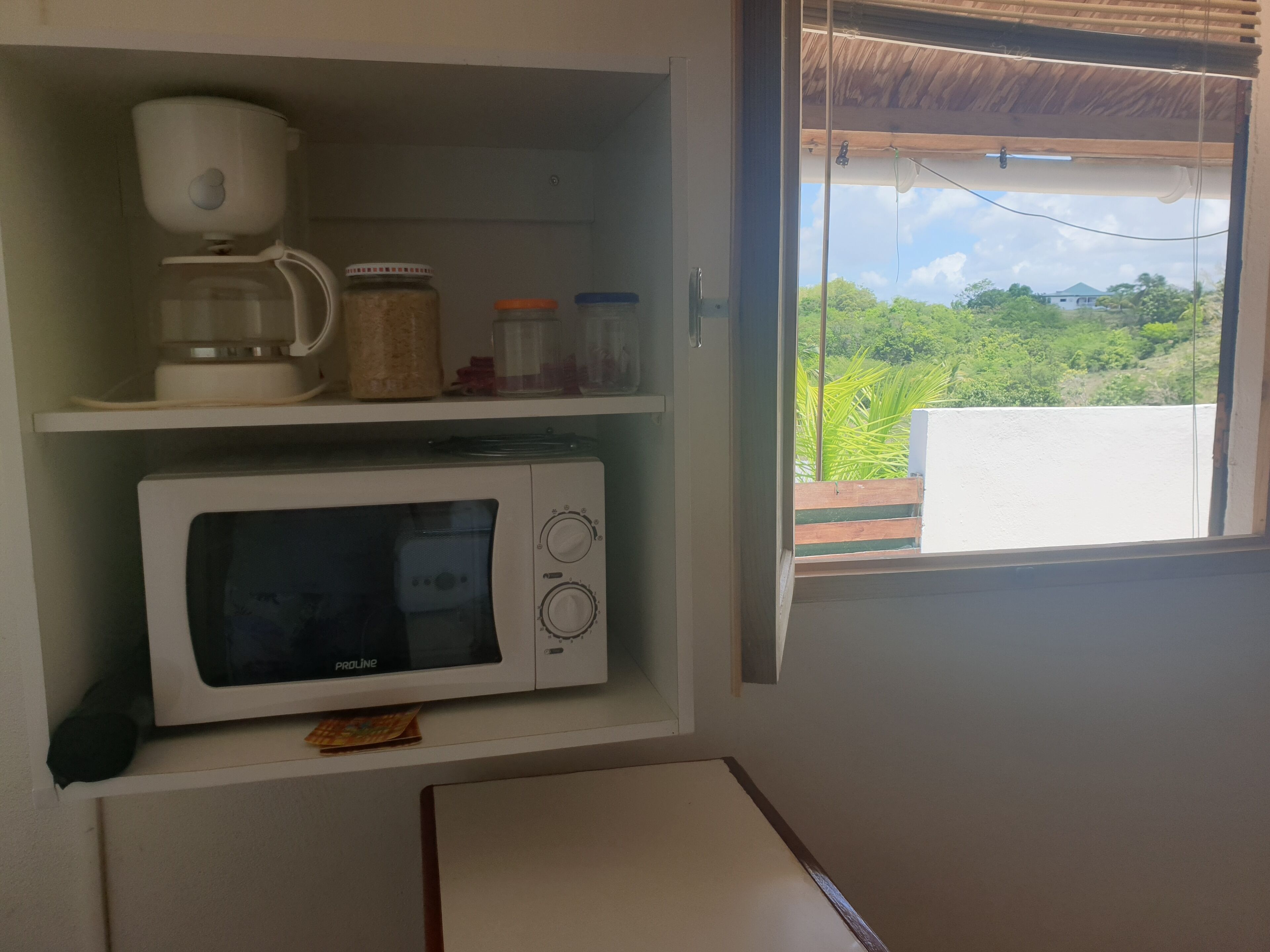 Una cocina con microondas blanco, cafetera y frascos en los estantes.