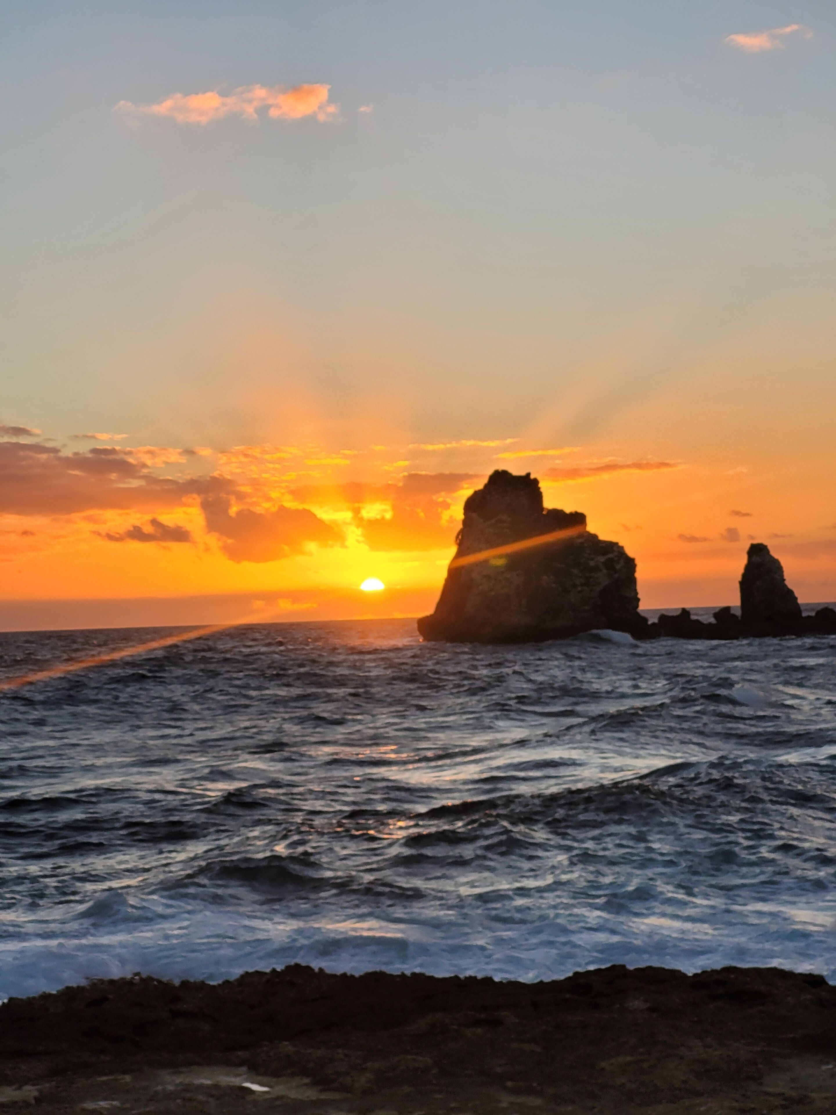 Een zonsondergang boven de oceaan met rotsformaties.