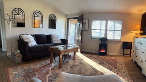 A living room with a sofa, coffee table, and a patterned rug. There is a fireplace, a lamp, and a window with blinds. - Mule Town Cottage, Historic Columbia TN. 3BR/2BA (Columbia)