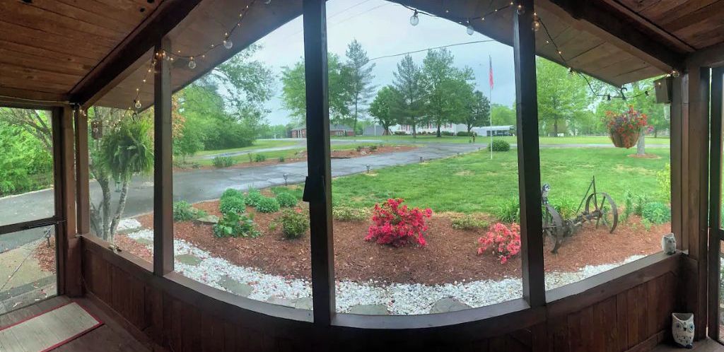 A covered porch with large windows overlooking a landscaped garden with red flowers and a swing set.