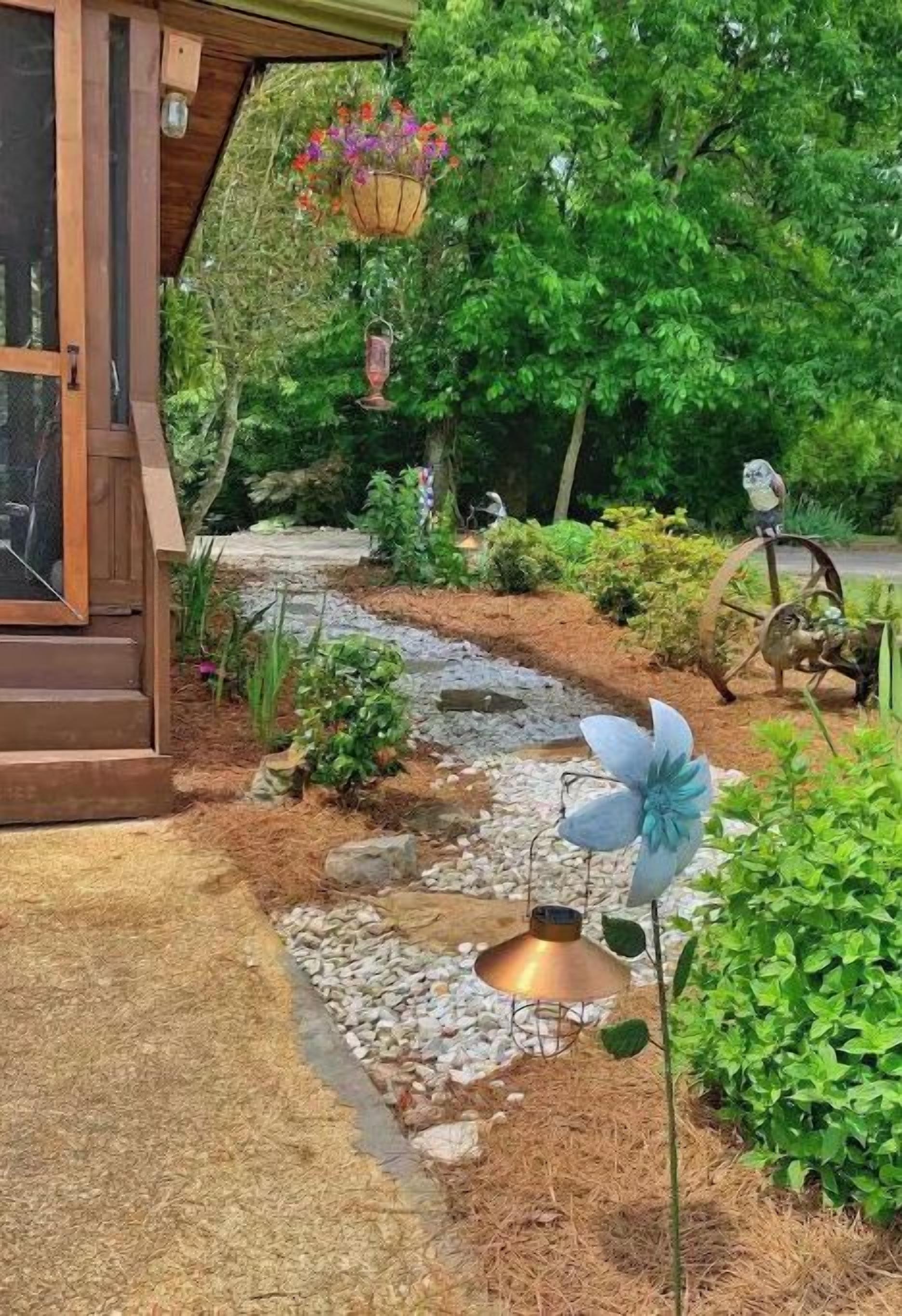 A garden pathway leading to a wooden structure with hanging flower baskets and a decorative metal lamp post.