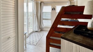 A staircase leading to a second floor with a wooden finish, a small kitchen area with a sink and countertop, and a view of the outside through large windows. - "The Turtle Nest" a 3bed/2 bath Condo in St Regis (New Listing) (North Topsail Beach)