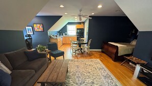 A cozy living room with a sofa, a coffee table, and a patterned rug. There is a dining area with a table and chairs, and a kitchen in the background. - Wandering Bear’s Den Private Studio Near Crozet and Charlottesville (Charlottesville)