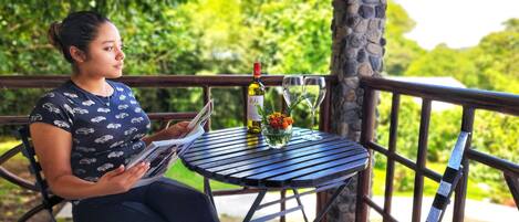 Une personne est assise à une petite table ronde, devant une bouteille de vin, un verre et un vase rempli de fleurs.
