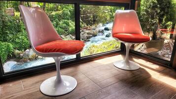 Dos sillas modernas con cojines rojos situadas junto a un ventanal grande que da a un jardín con un arroyo.