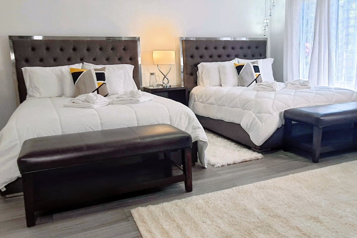 A hotel room with two beds, a bench, a nightstand, and a lamp.