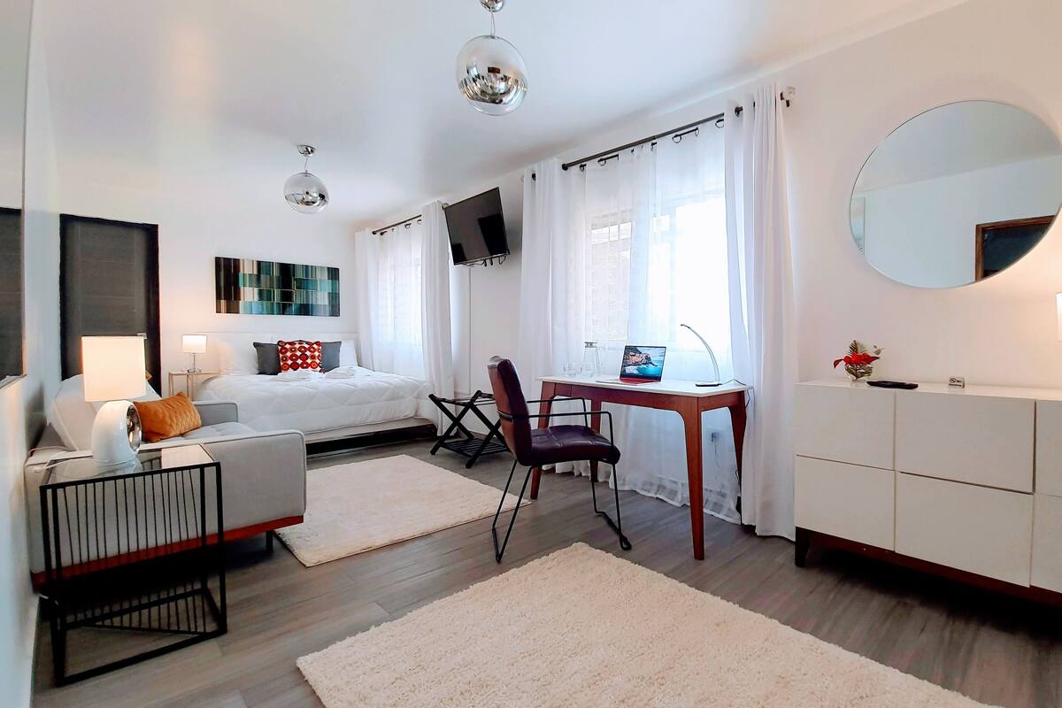A modern hotel room with a bed, desk, chair, and a large mirror.