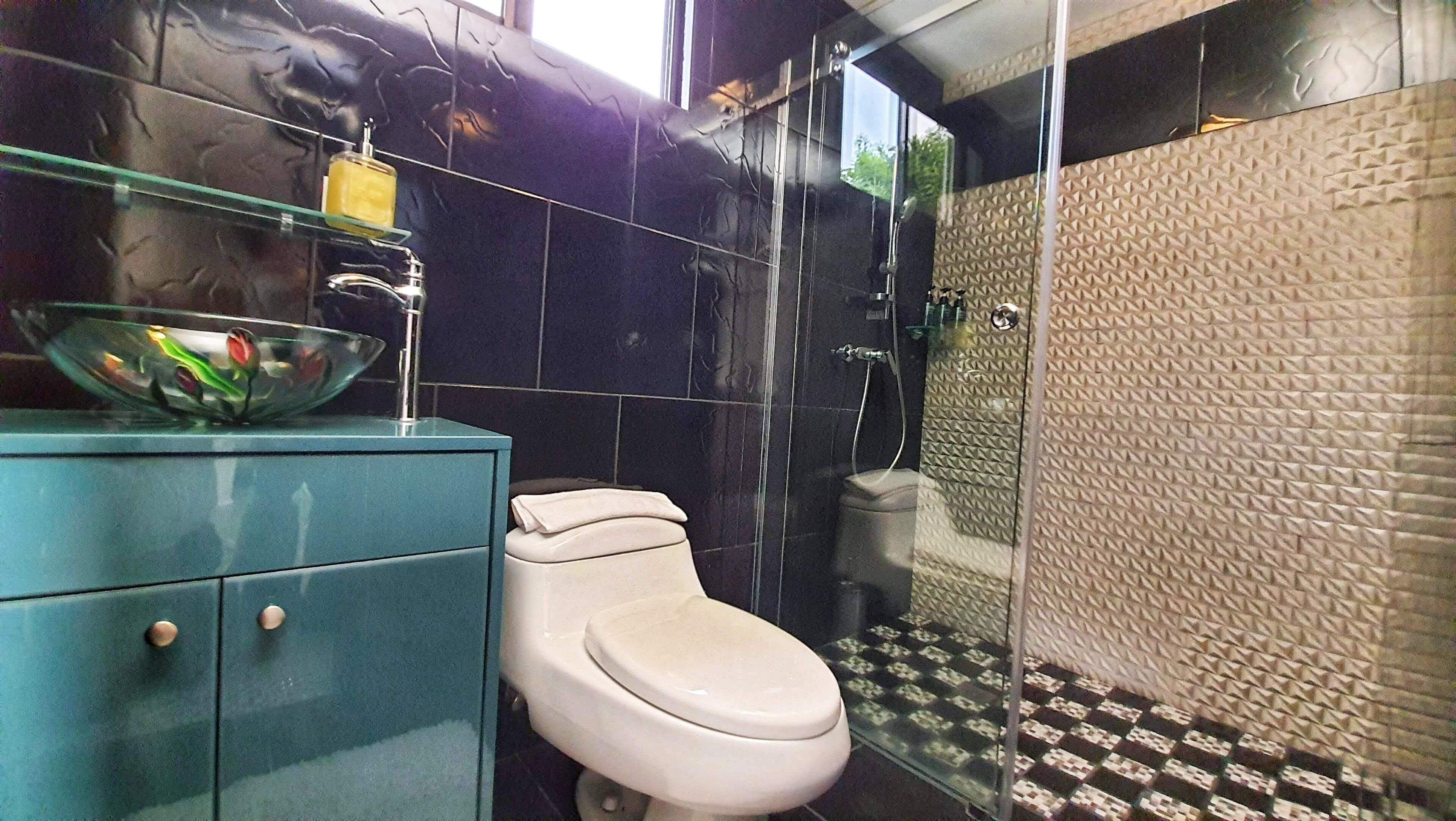 Une salle de bain comprenant des toilettes, un lavabo en verre et un espace douche avec des murs à texture.