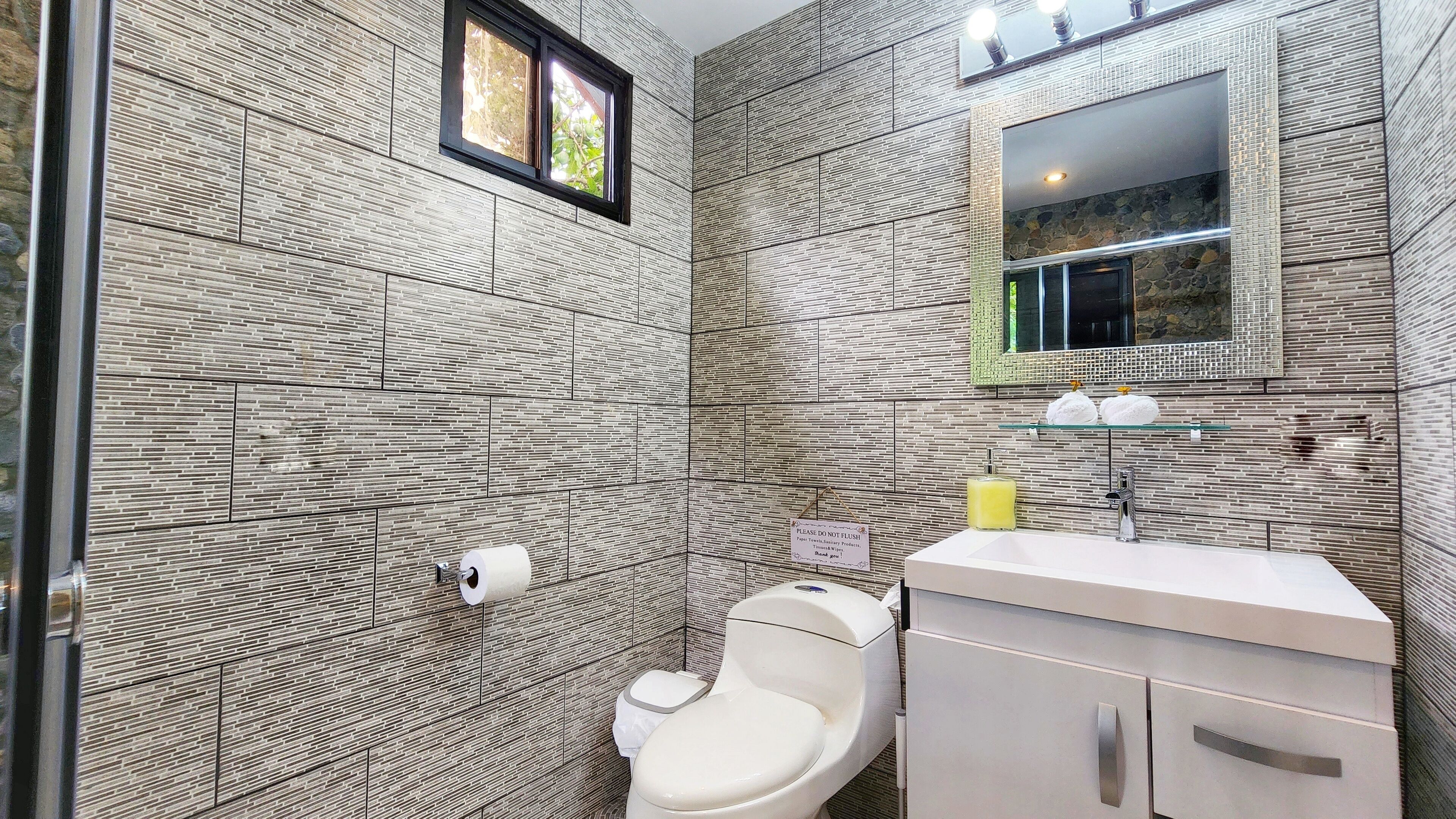 A modern bathroom with a tiled wall, a toilet, a sink, and a mirror.