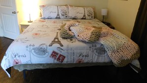 Un lit avec une couette aux motifs parisiens, une couverture tricotée et des coussins assortis.